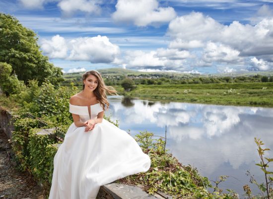 6S2A2590 Patrick bride sitting on wall with water in the background and land with sky in view